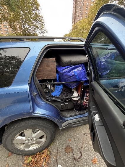 A blue car's back seat and floor are dangerously overstuffed with unsecured luggage, illustrating unsafe packing for a move or long trip